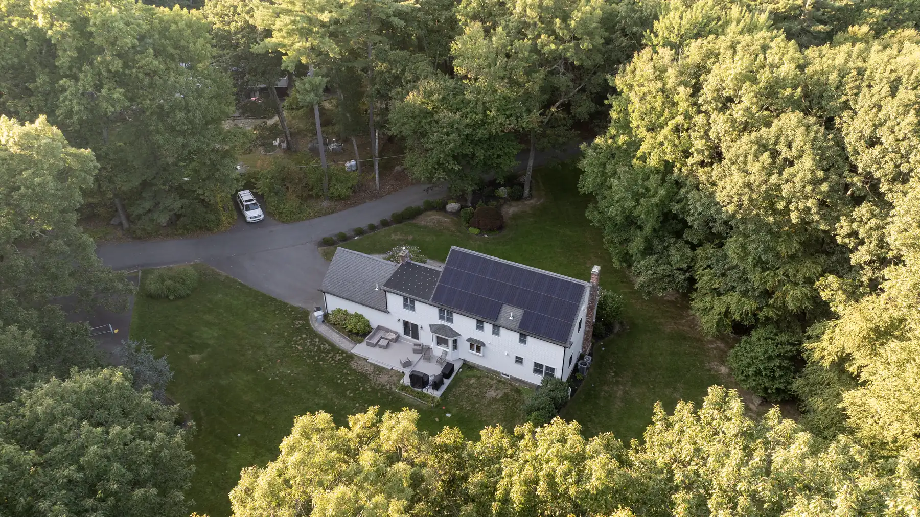 Aerial view of a white two-story home surrounded by trees and lawn.