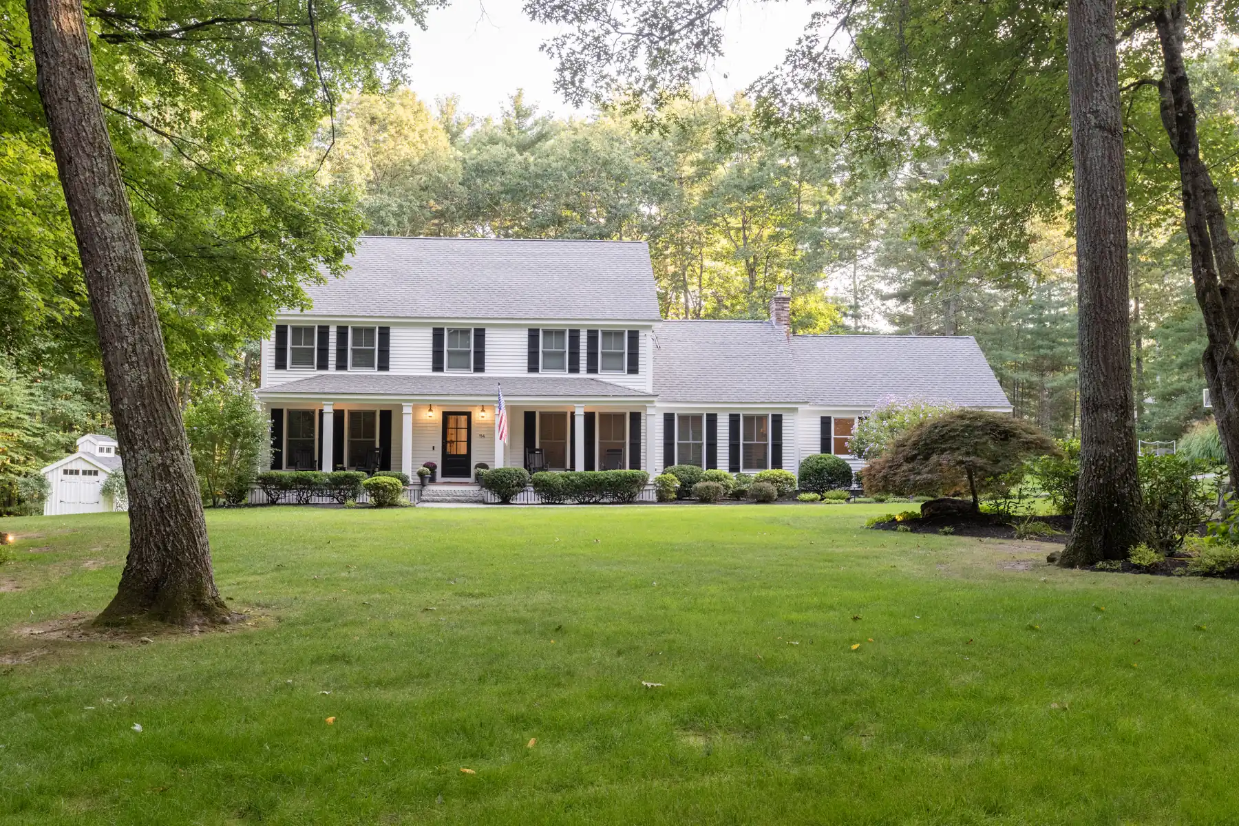 Front exterior of a white two-story home framed by mature trees.
