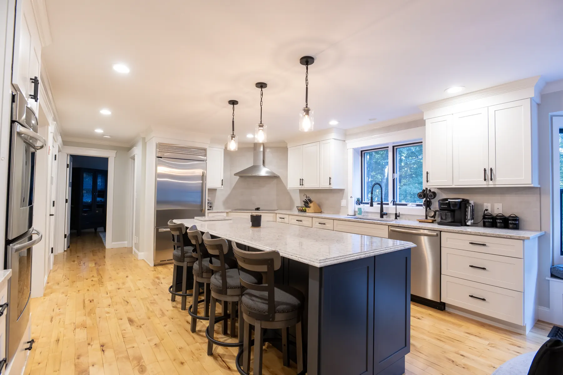 White kitchen with a dark island, stone counters, and pendant lighting.