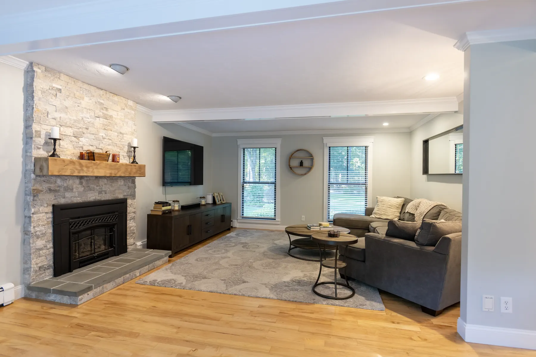 Open living room with a stone fireplace, sectional seating, and hardwood floors.