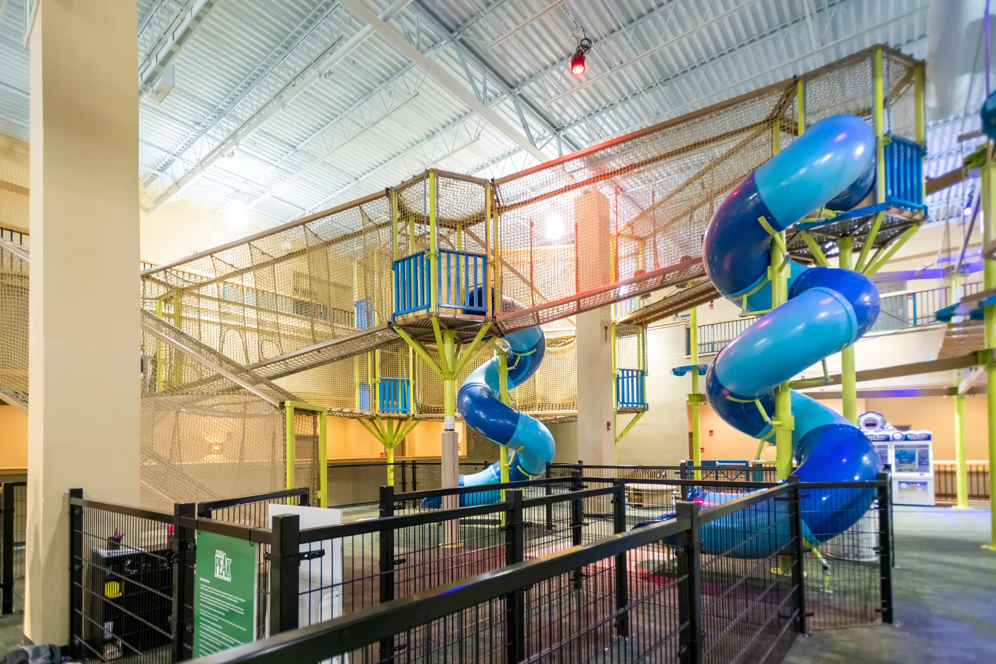 Wide interior view of a multilevel adventure park with blue tube slides and suspended courses.