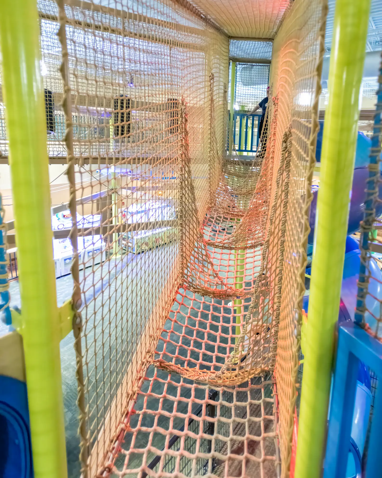 Interior of a netted obstacle path with hanging rope panels and a wooden walkway.