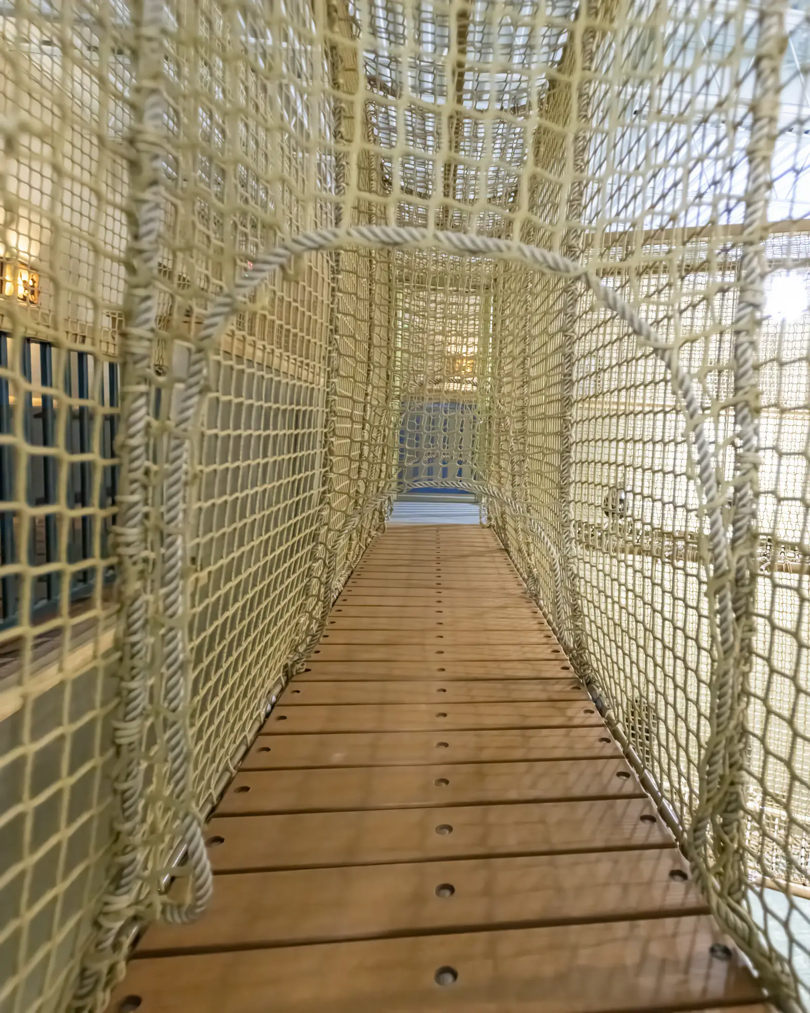 Wood-plank walkway enclosed by rope netting inside the adventure course.