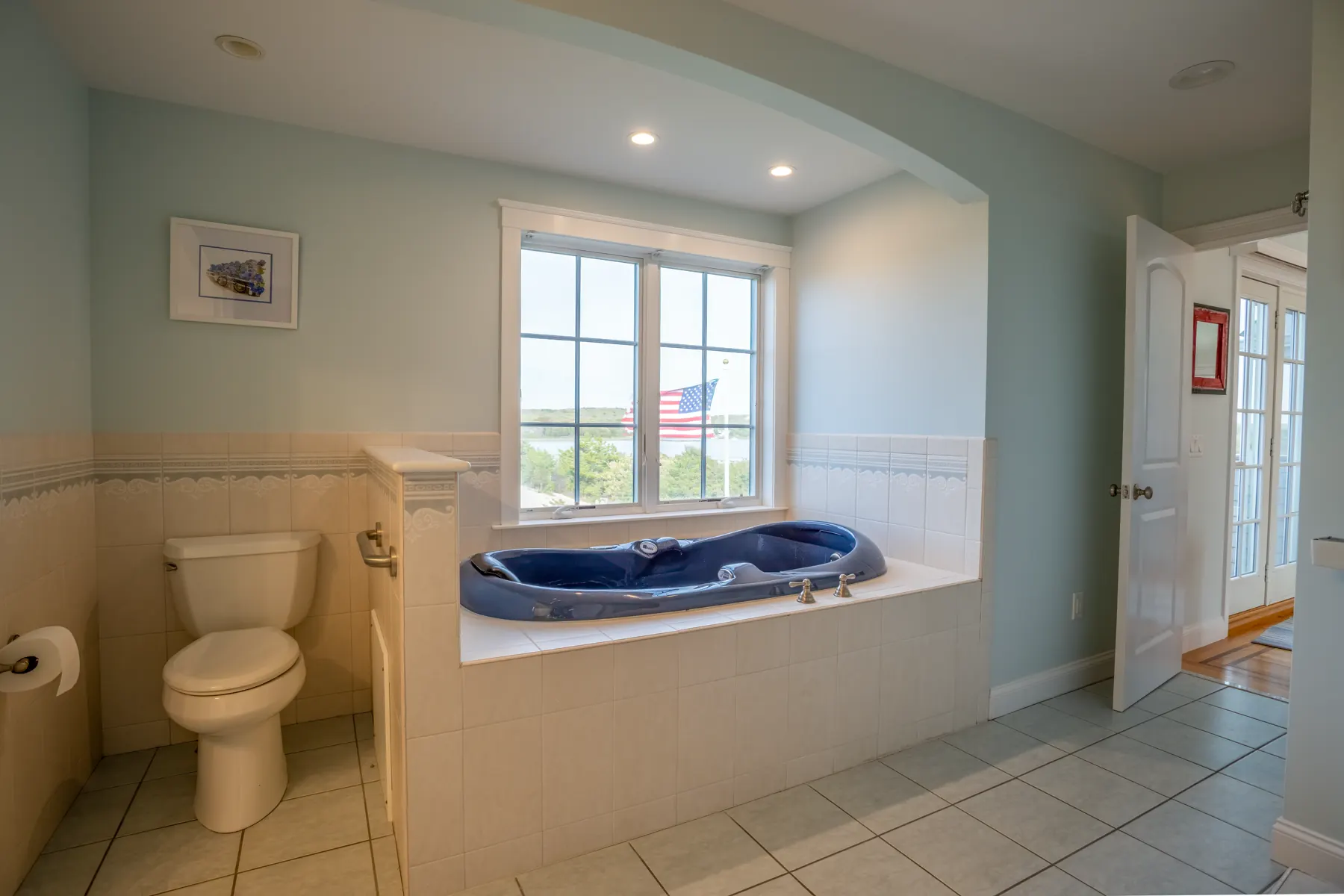 Blue soaking tub set beneath windows with a coastal view.