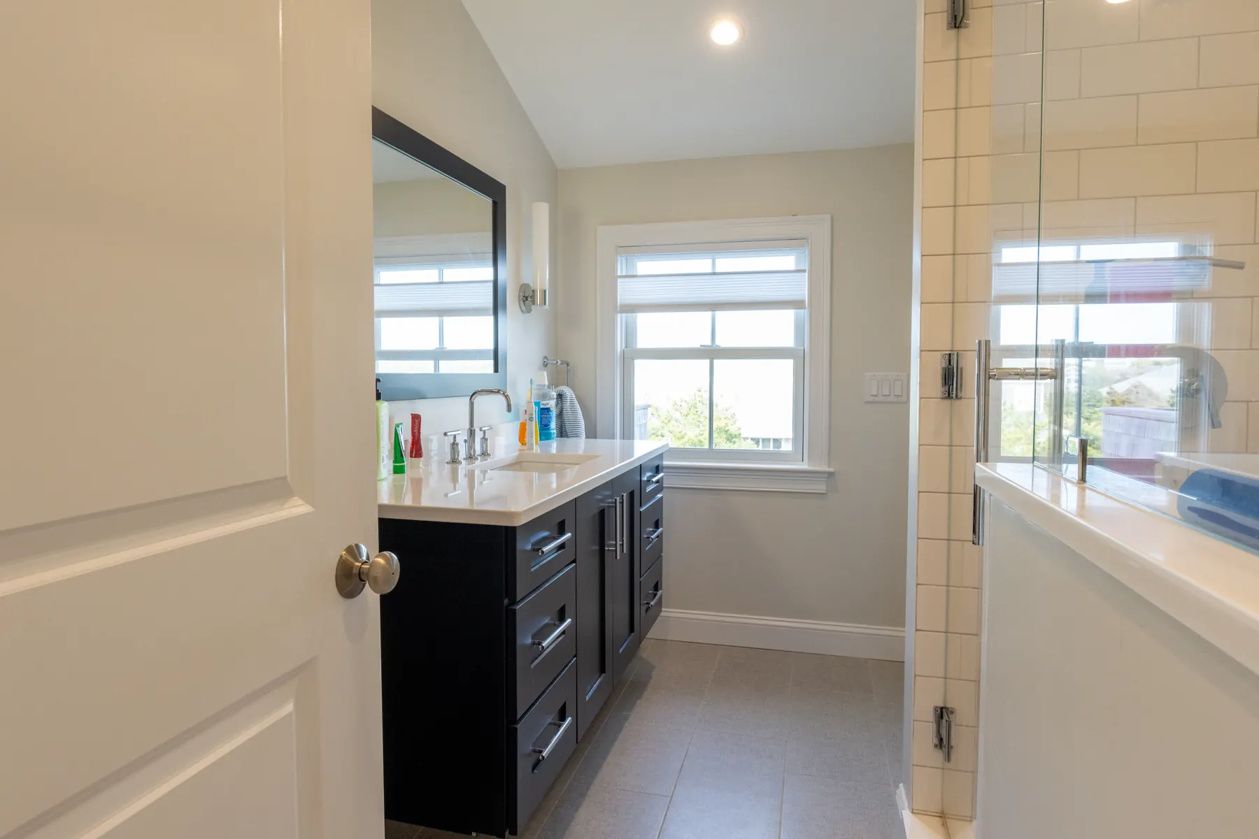 Bright bathroom with a dark double vanity and glass shower.