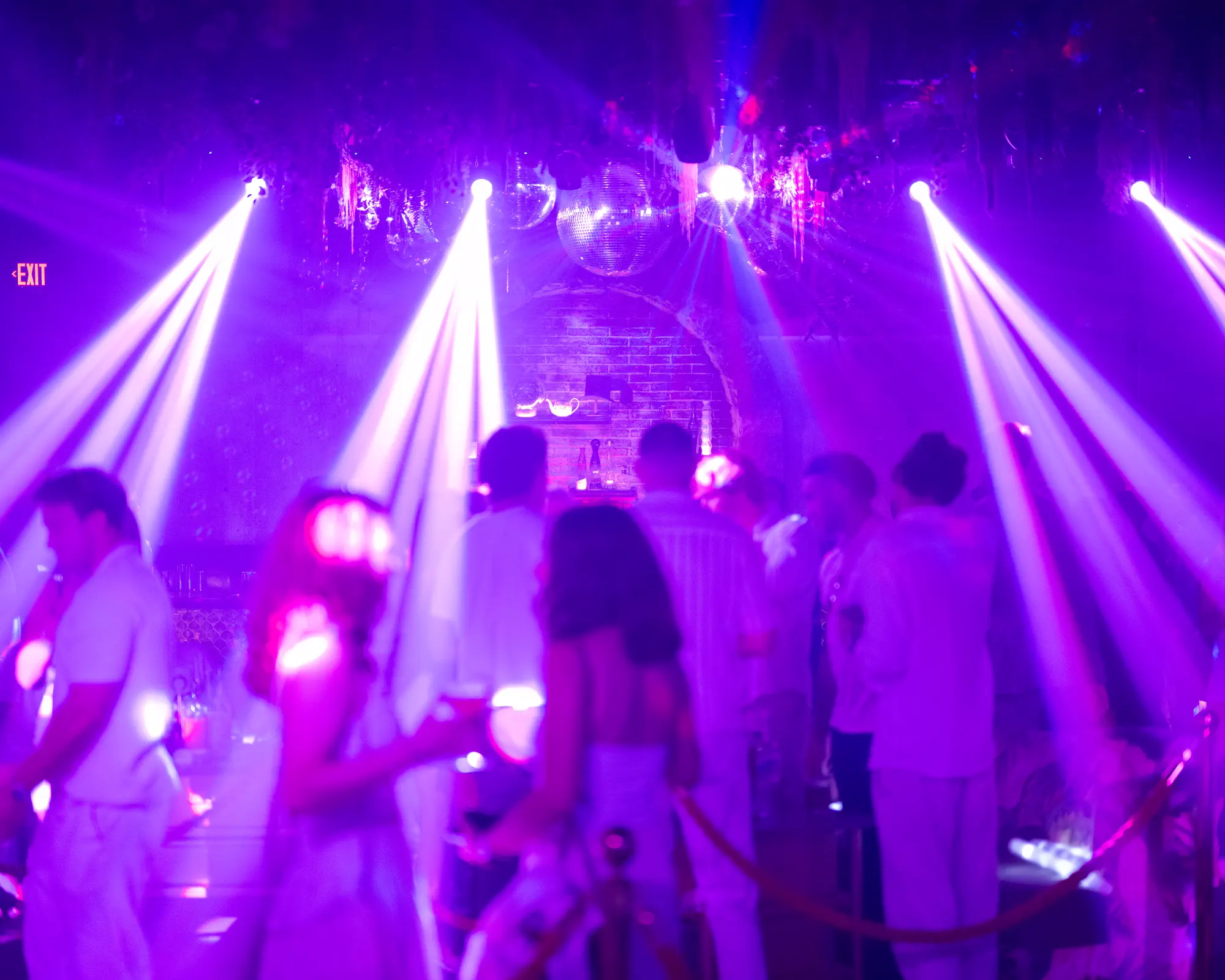 Nightclub crowd gathered beneath purple spotlights and mirrored disco balls.