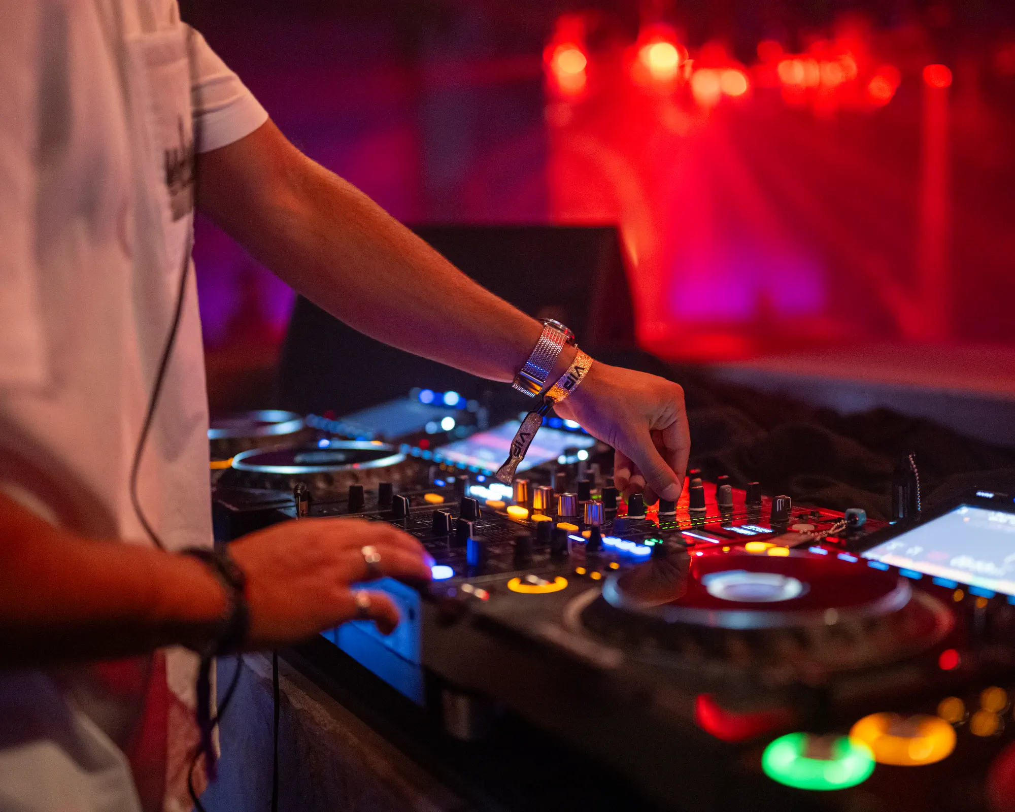 Close view of a DJ adjusting controls on a lit mixing console.
