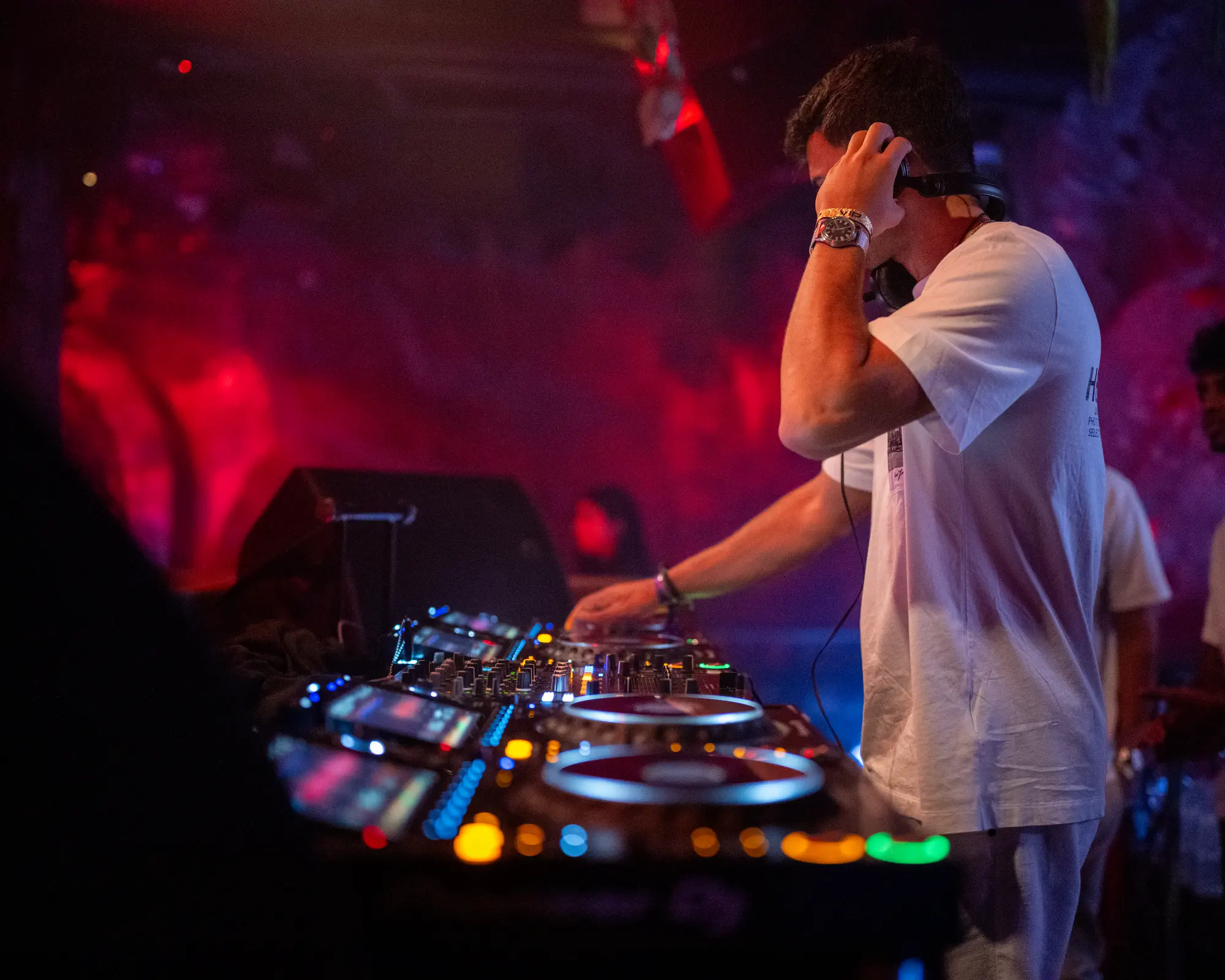 DJ working at the booth under red nightclub lighting.
