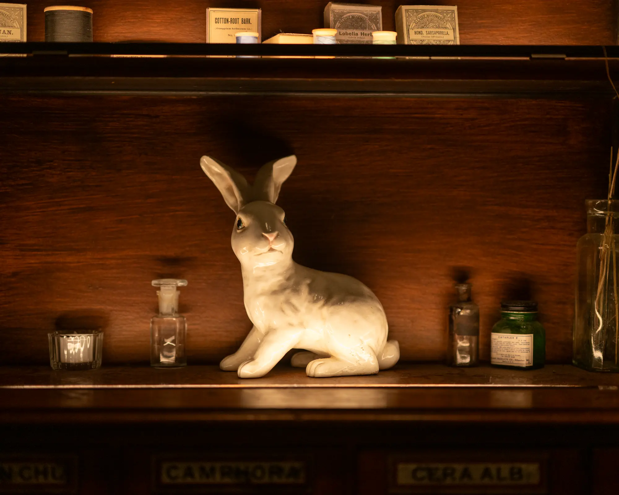 Rabbit sculpture displayed among bottles on a dark wood shelf.