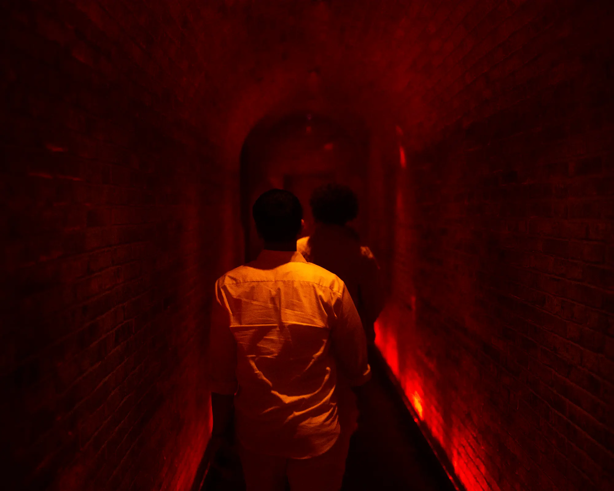 Guest walking through a narrow brick tunnel lit in red.