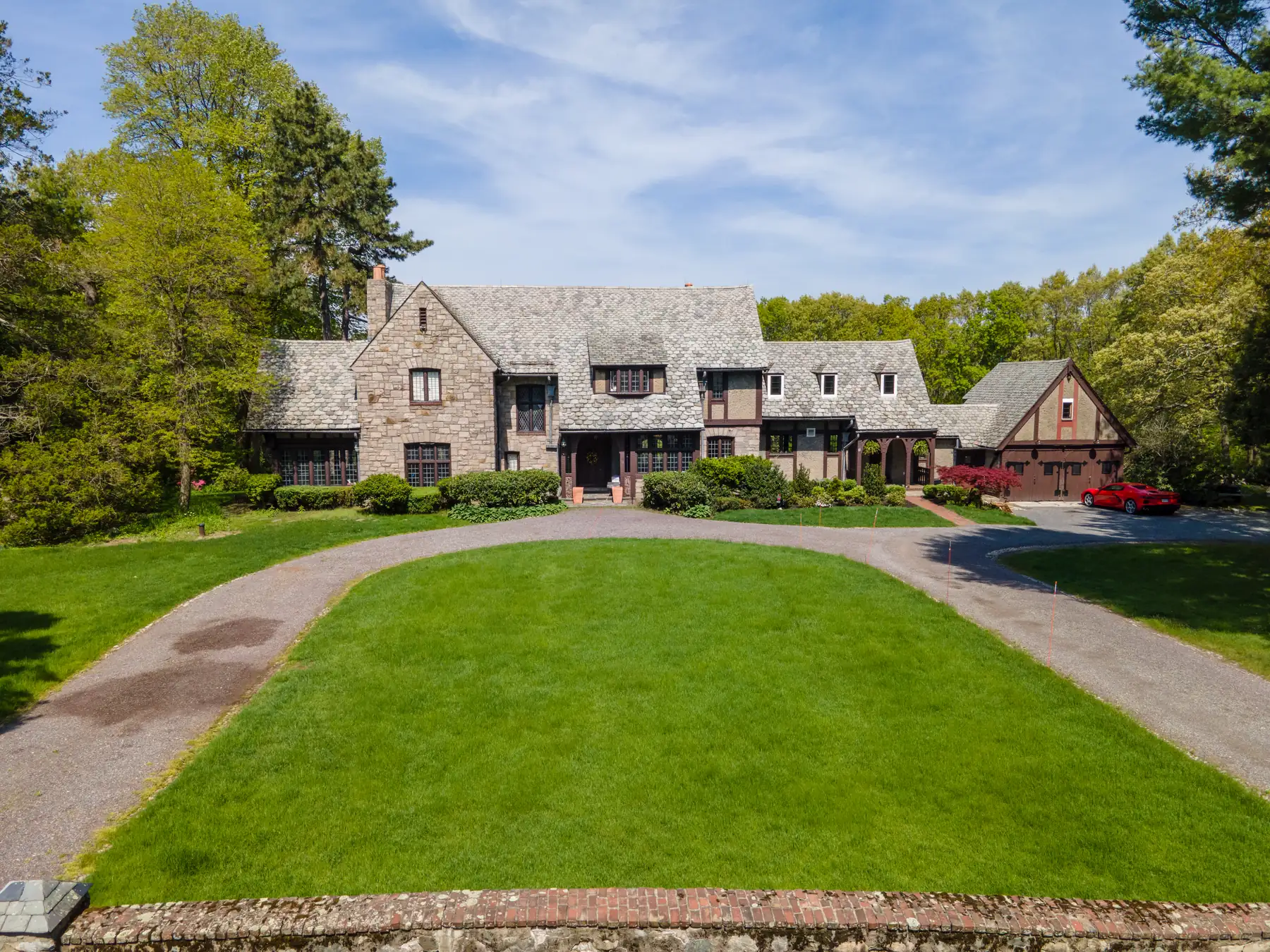 Front view of a stone-and-timber English Tudor home framed by mature trees.
