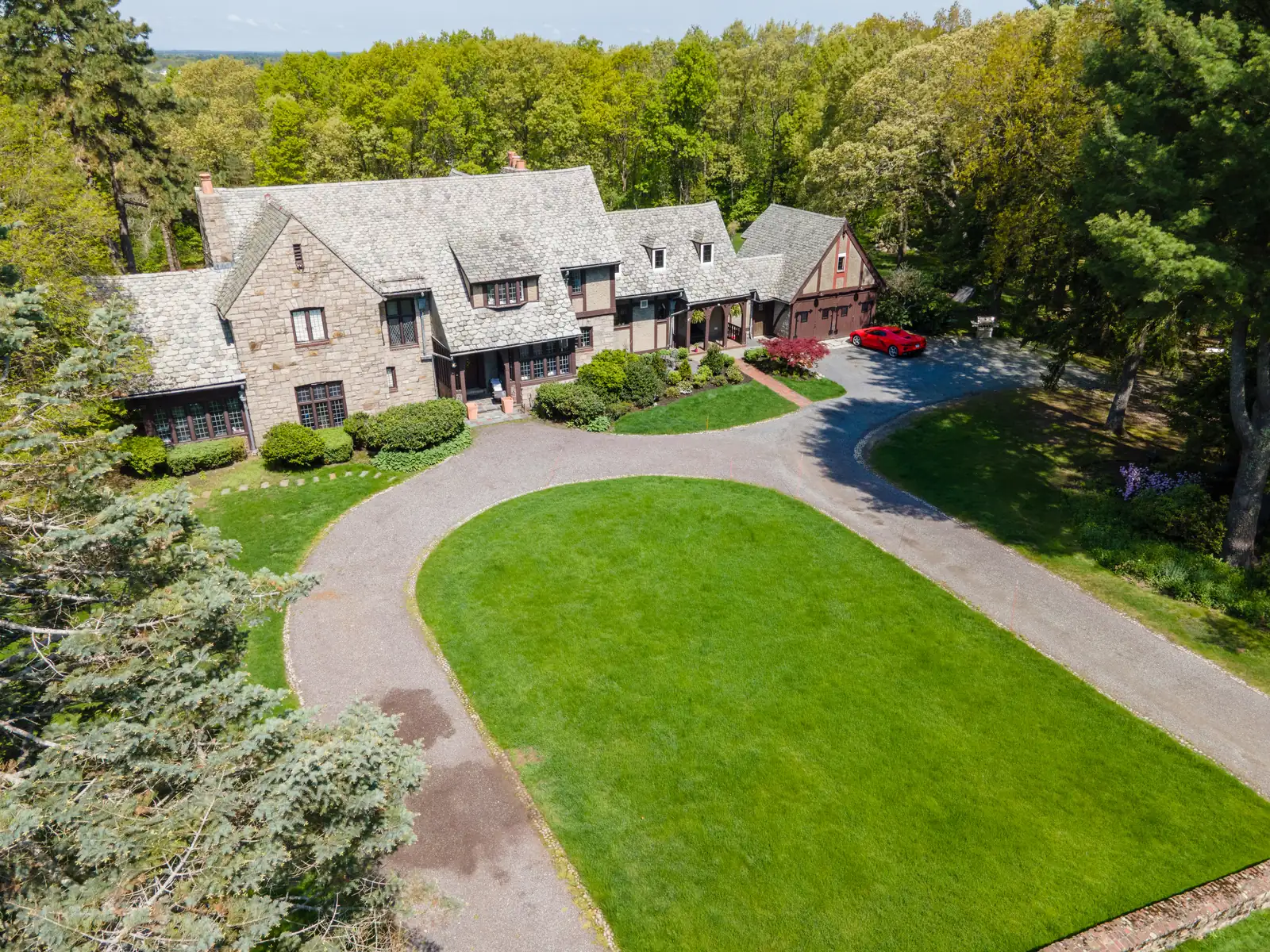 Angled aerial view of the Tudor home's front facade and circular lawn.
