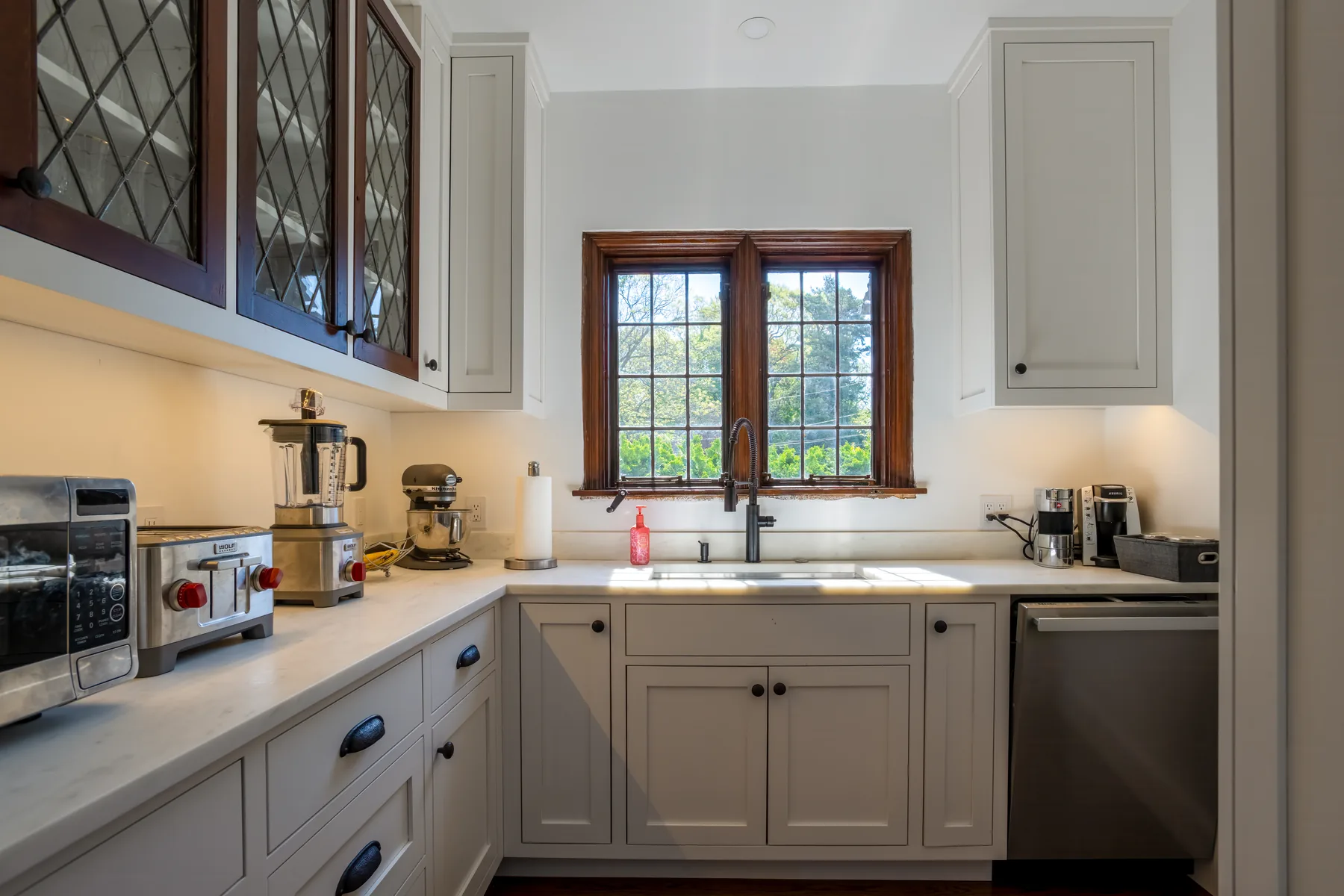 Compact gray pantry with stone counters and a leaded window.