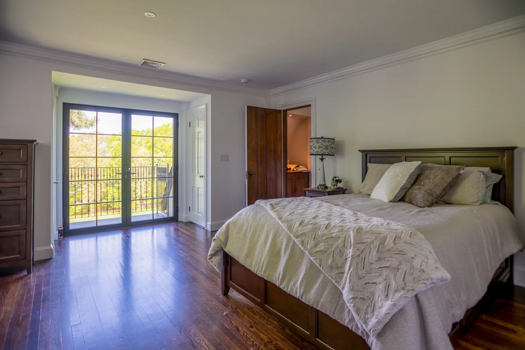 Primary bedroom with dark wood floors and French doors opening to a balcony.