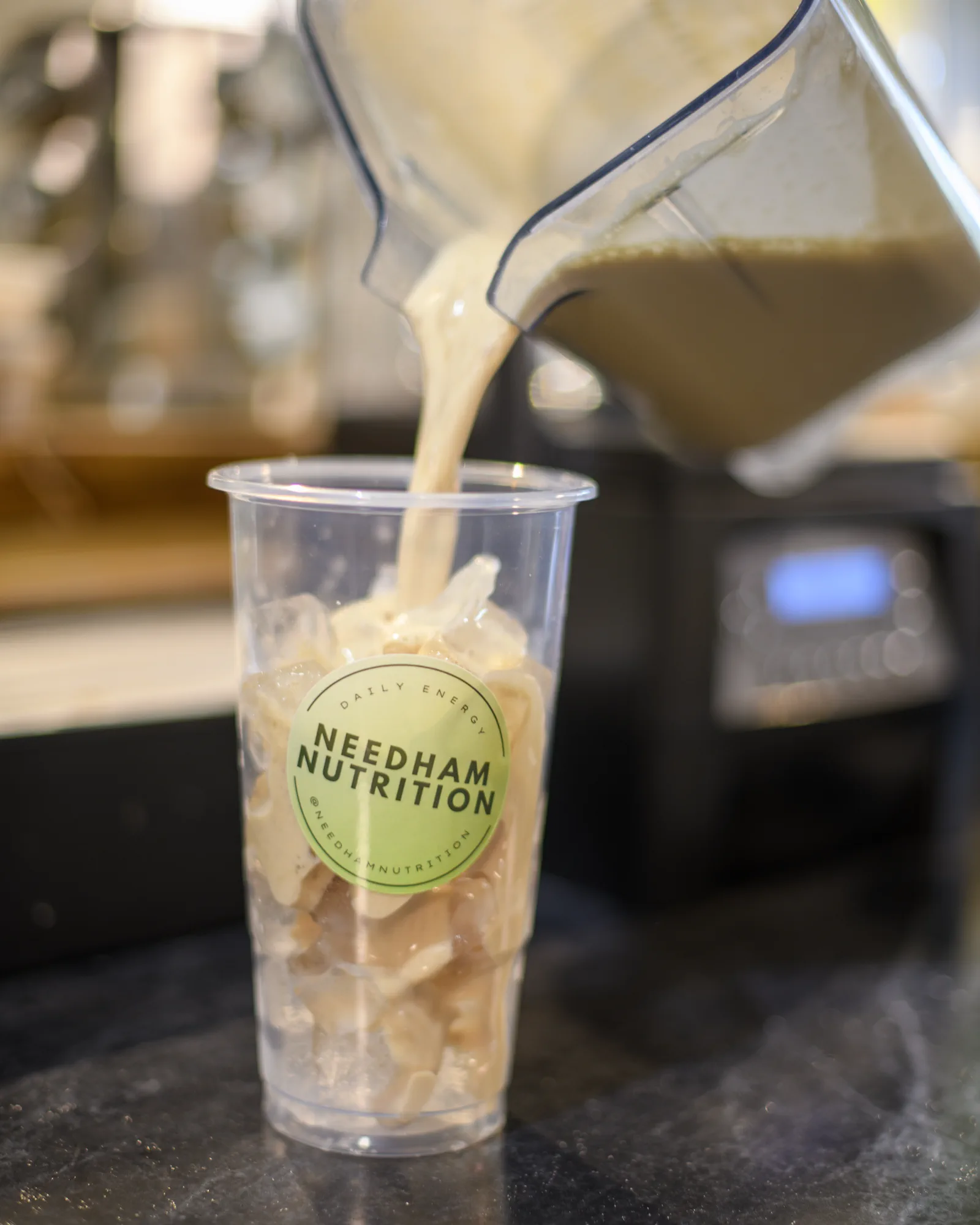 Blended drink being poured over ice into a Needham Nutrition cup.