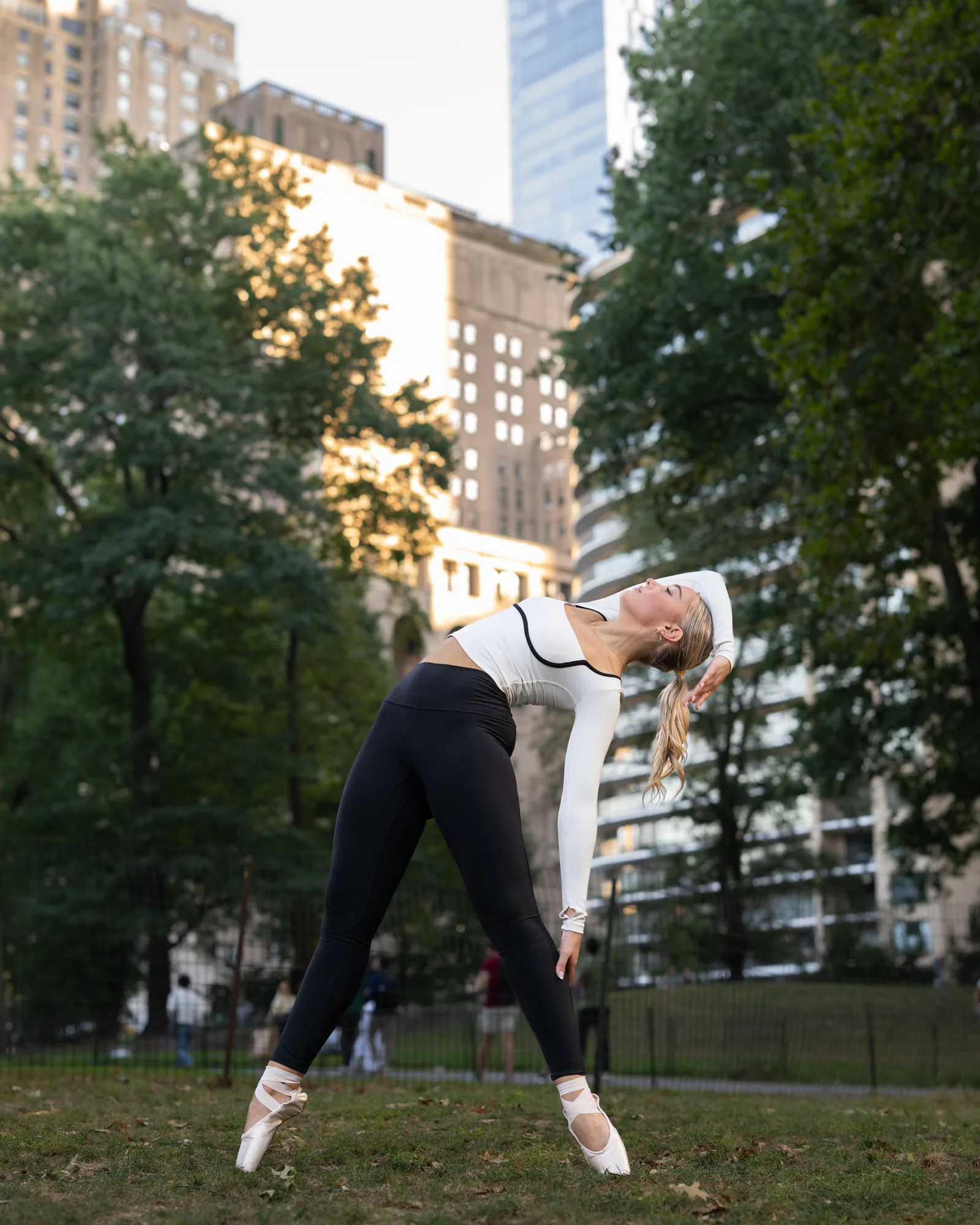 Dancer stretching into a side bend on pointe in a New York City park.