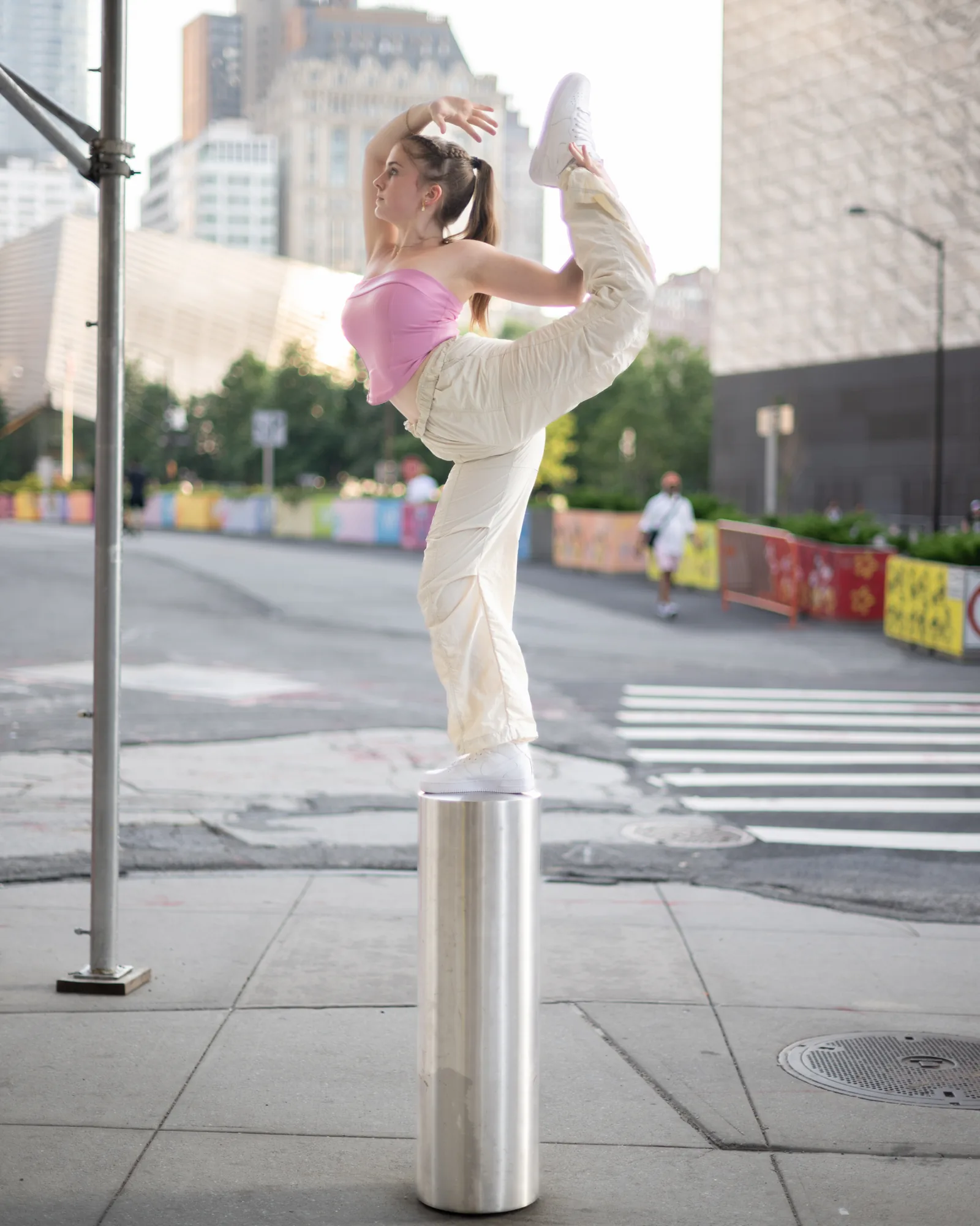 Dancer holding a high leg balance while standing on a metal bollard in New York City.