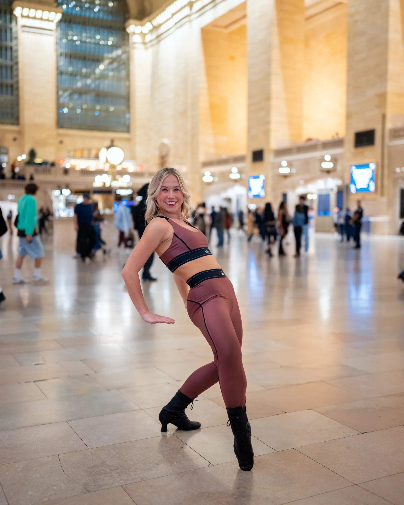 Dancer balancing with one knee raised on a New York City train terminal concourse.