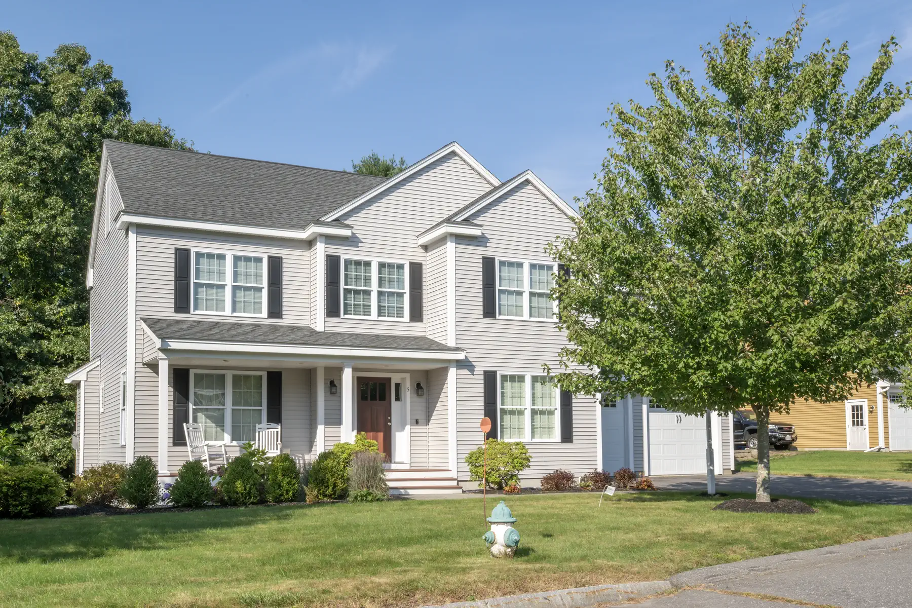 Front exterior of a gray two-story home with black shutters, a covered porch, and an attached garage.