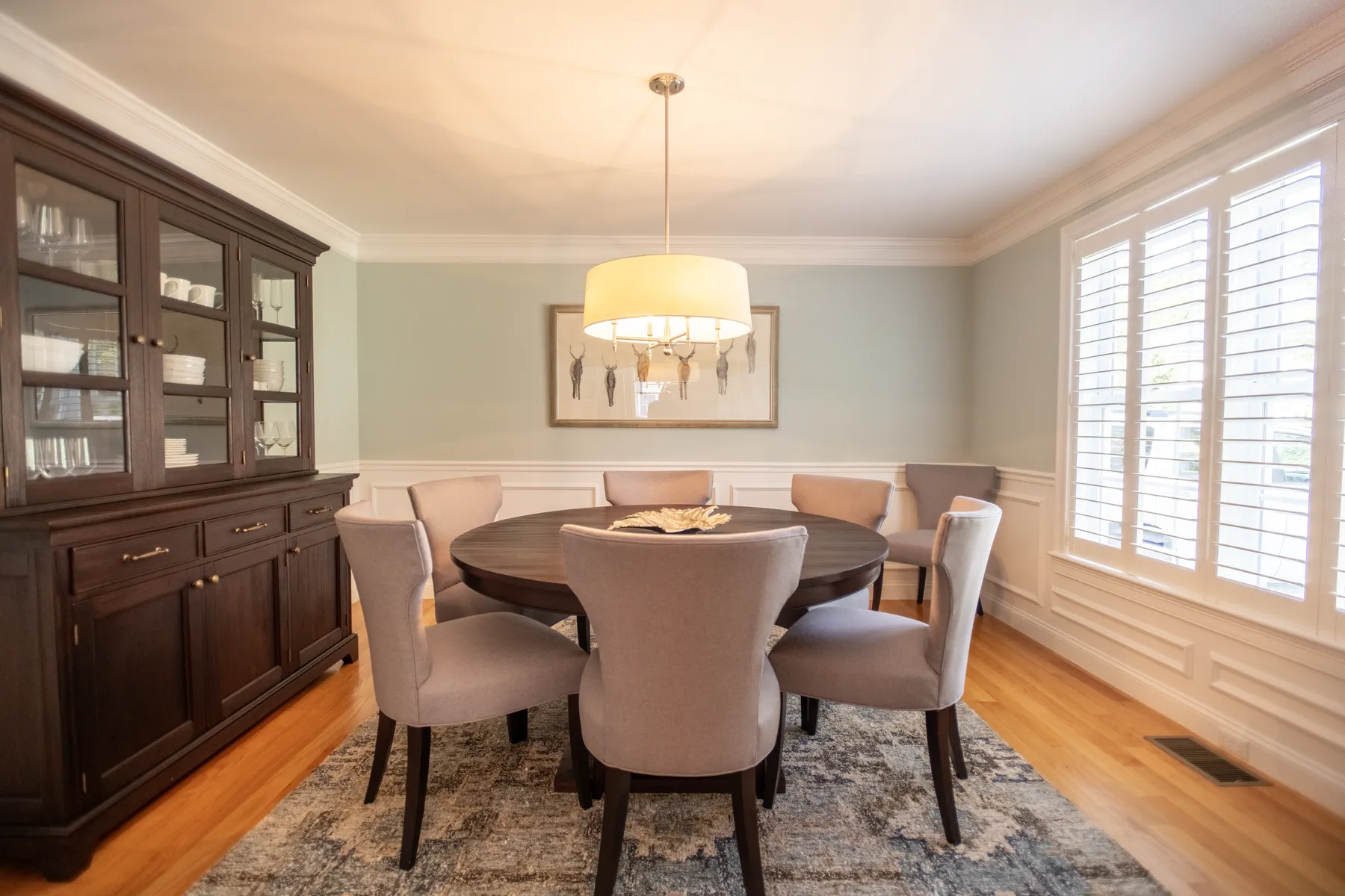 Formal dining room with a dark wood table, built-in hutch, chandelier, and shuttered windows.