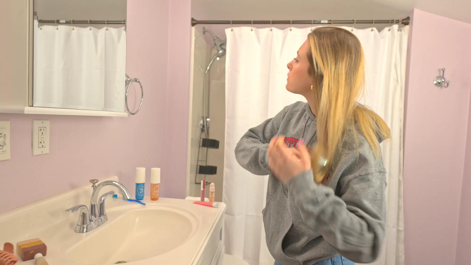 Woman getting ready at a pink bathroom mirror.