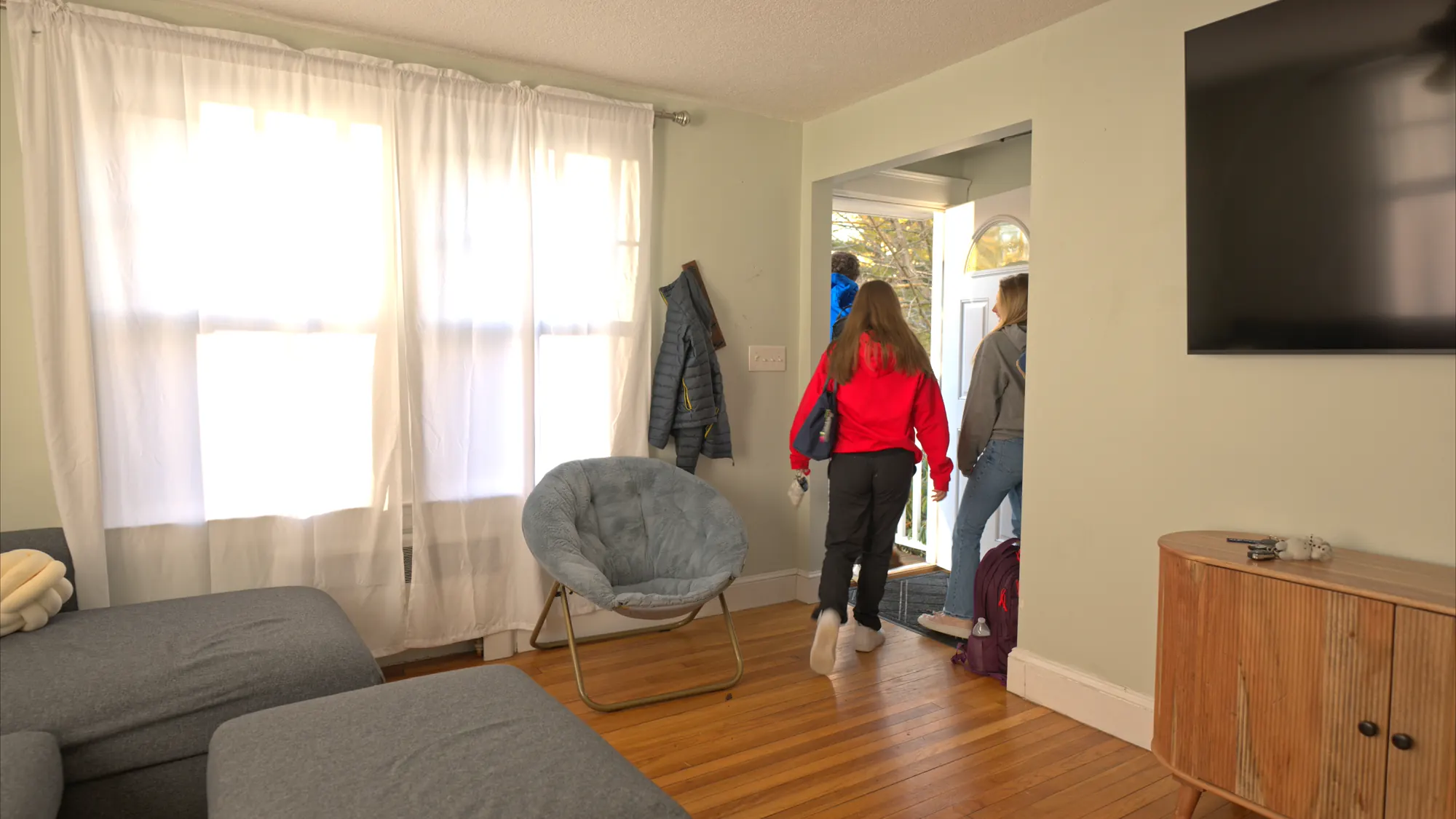Woman walking toward the front door of a furnished living room.