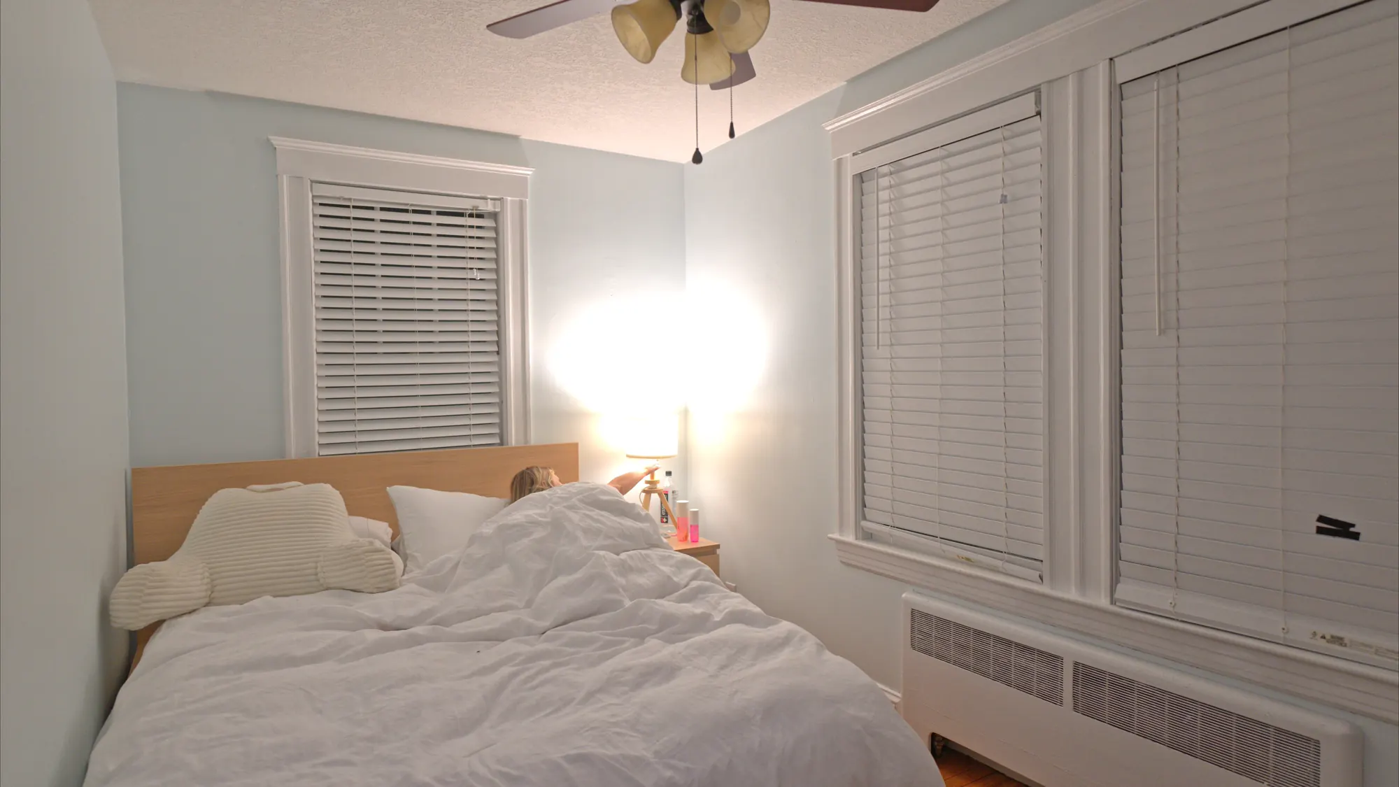 Bedroom at night with a rumpled bed and a glowing bedside lamp.