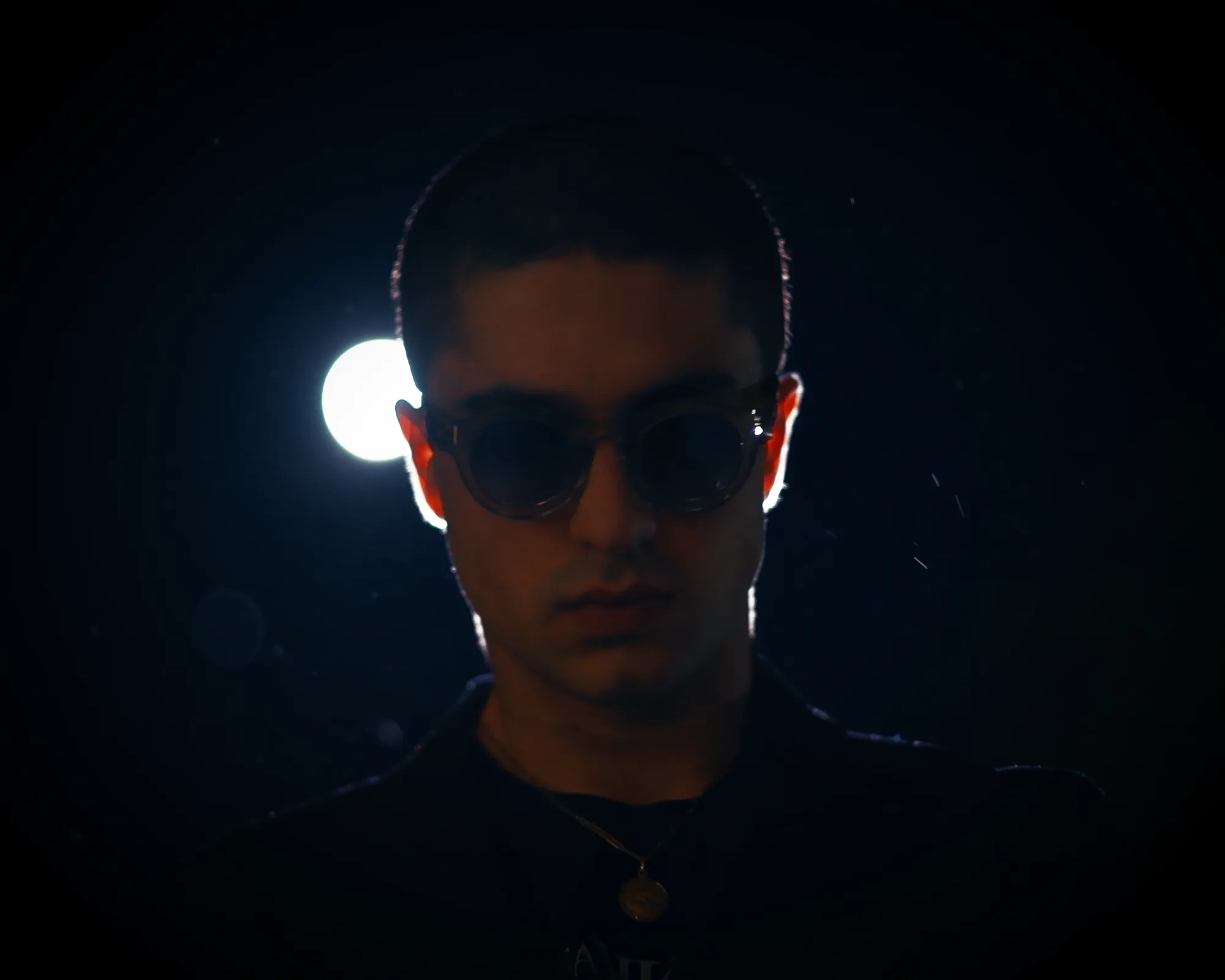 Low-key portrait of the TAKKRA founder wearing sunglasses beneath a spotlight.