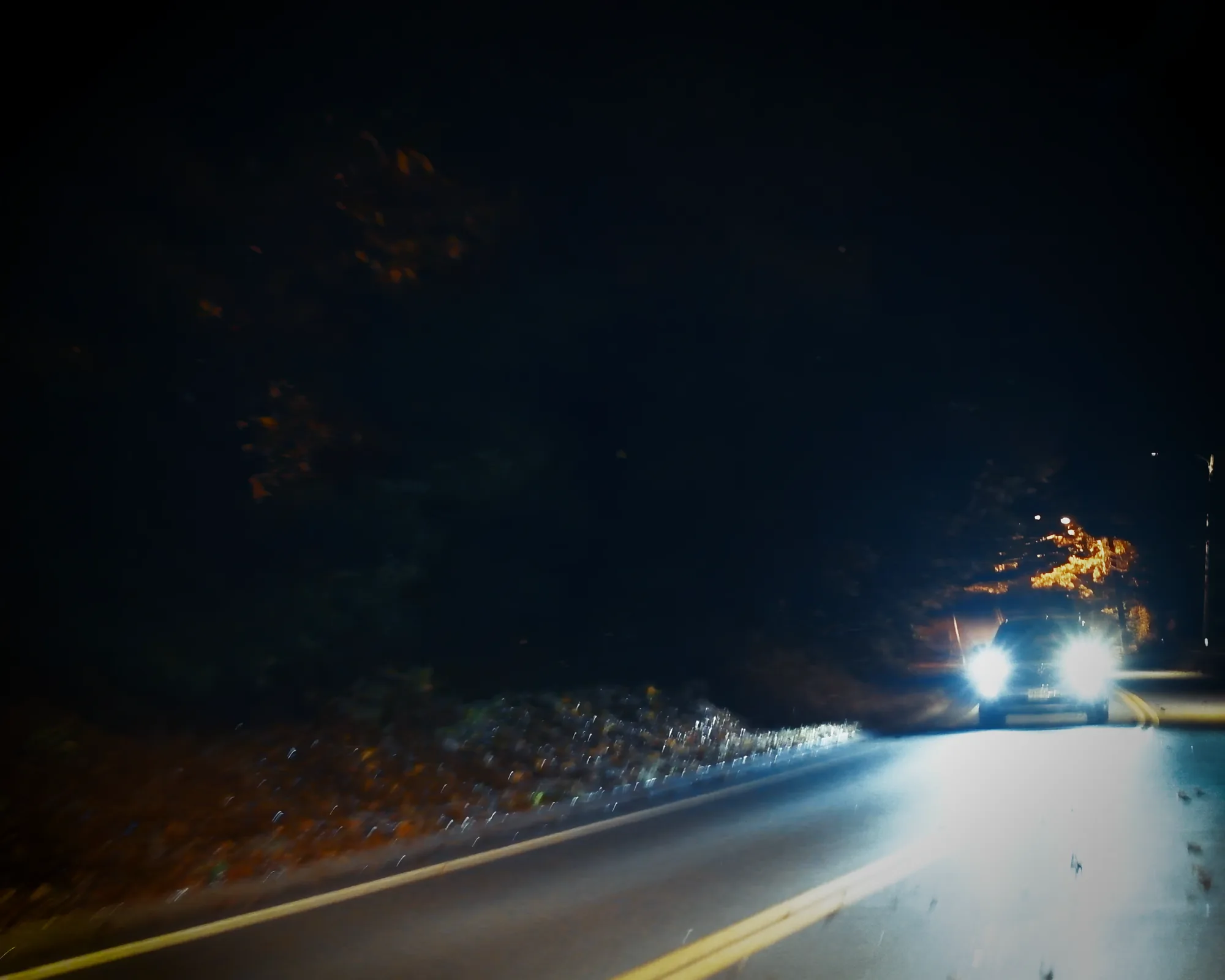 Car headlights illuminating a winding road at night.