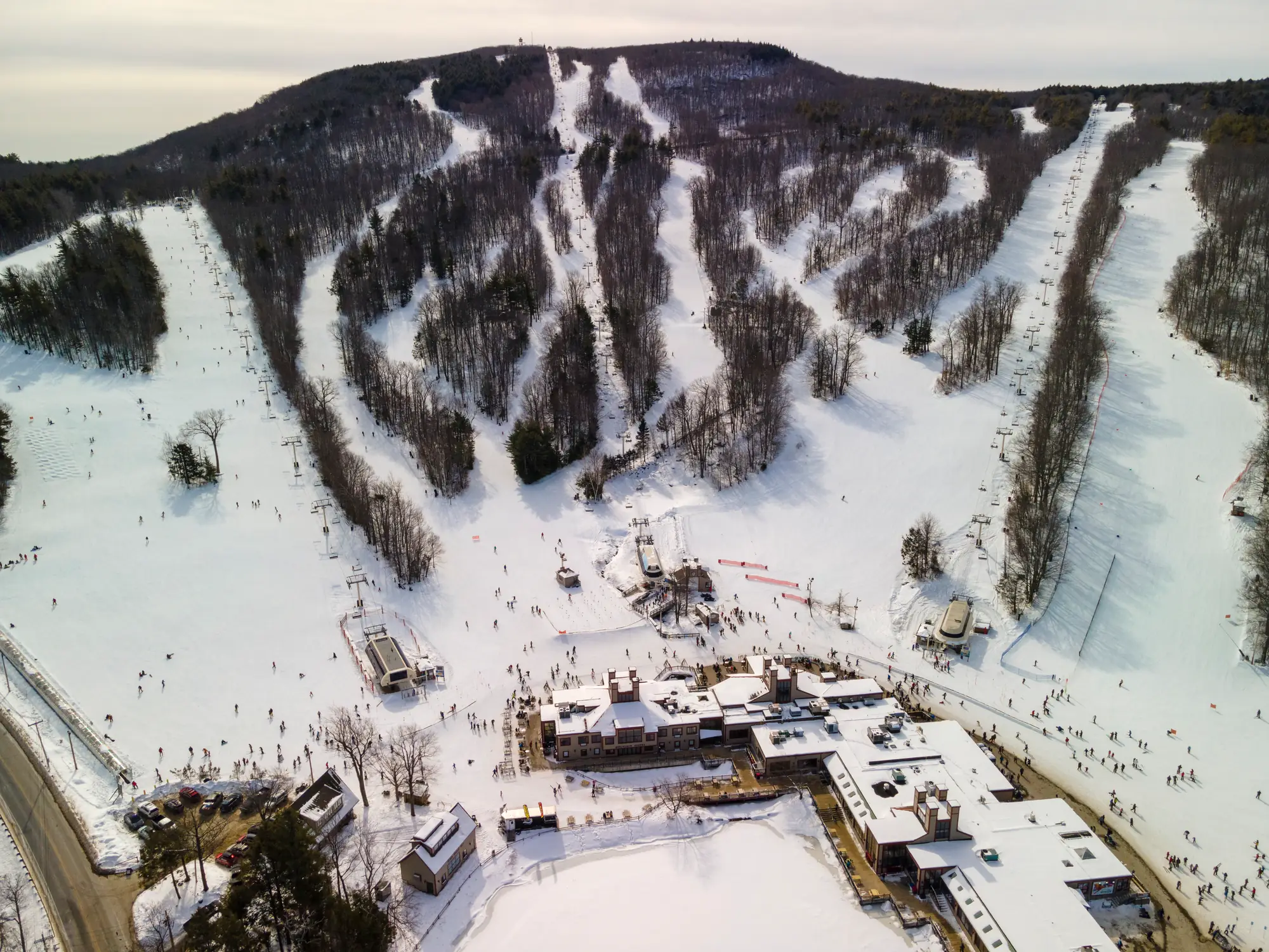 Aerial view of a snow-covered mountain resort with ski trails, chair lifts, and base buildings.